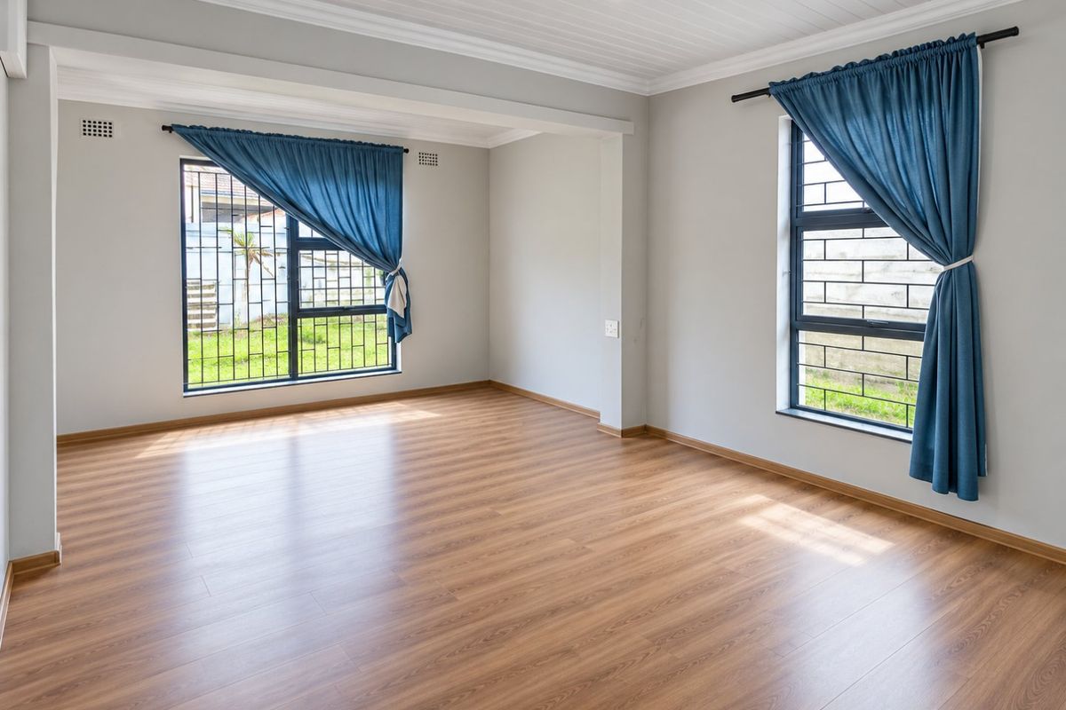 A bright, empty living room featuring modern laminate flooring, tongue and groove ceiling details, and large windows fitted with security bars.
