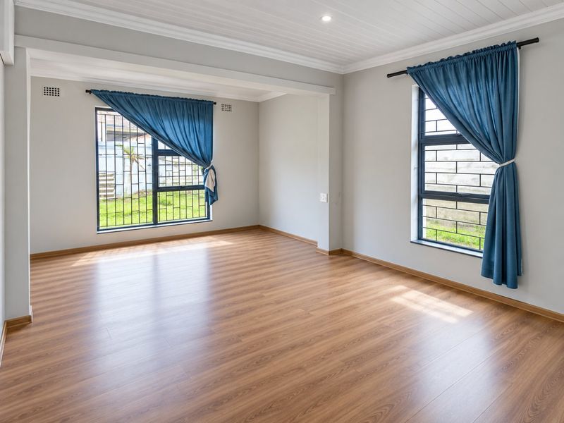 A bright, empty living room featuring modern laminate flooring, tongue and groove ceiling details, and large windows fitted with security bars.
