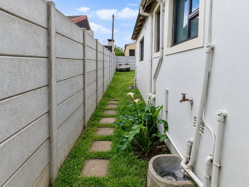 A narrow side garden path featuring a precast concrete boundary wall, paved stepping stones, and external utility fixtures including a water tap and drainage gully.