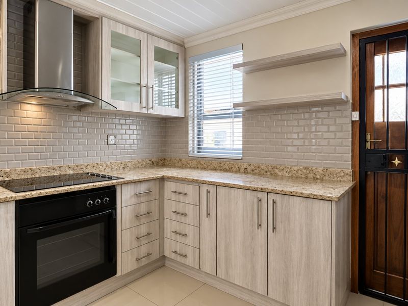 Modern kitchen featuring light wood-grain cabinetry, granite countertops, subway tile backsplash, and integrated stainless steel appliances with a secure exterior door.