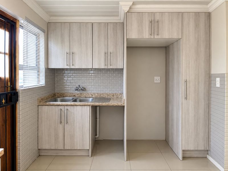 A clean and functional scullery featuring light wood-grain cabinetry, granite countertops, a double sink, and a subway tile backsplash.