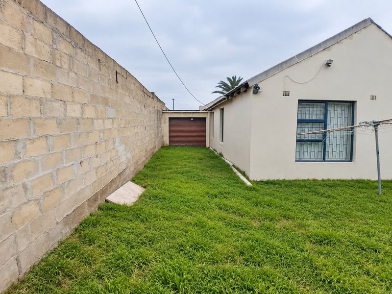 Rear exterior view showing a grassed yard, boundary wall, and access to a single garage with a roller door.