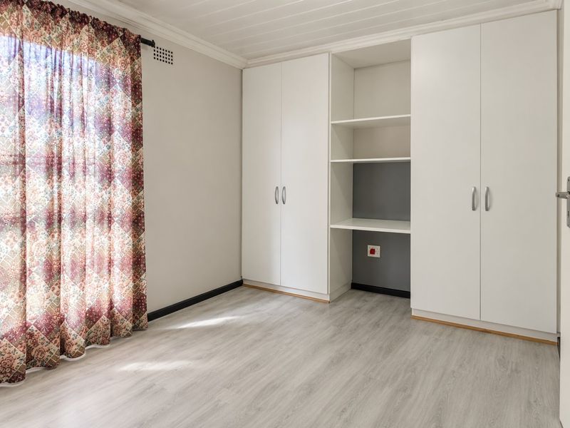A bright, empty bedroom featuring modern laminate flooring, a white tongue and groove ceiling, and ample built-in cupboard storage with integrated shelving.