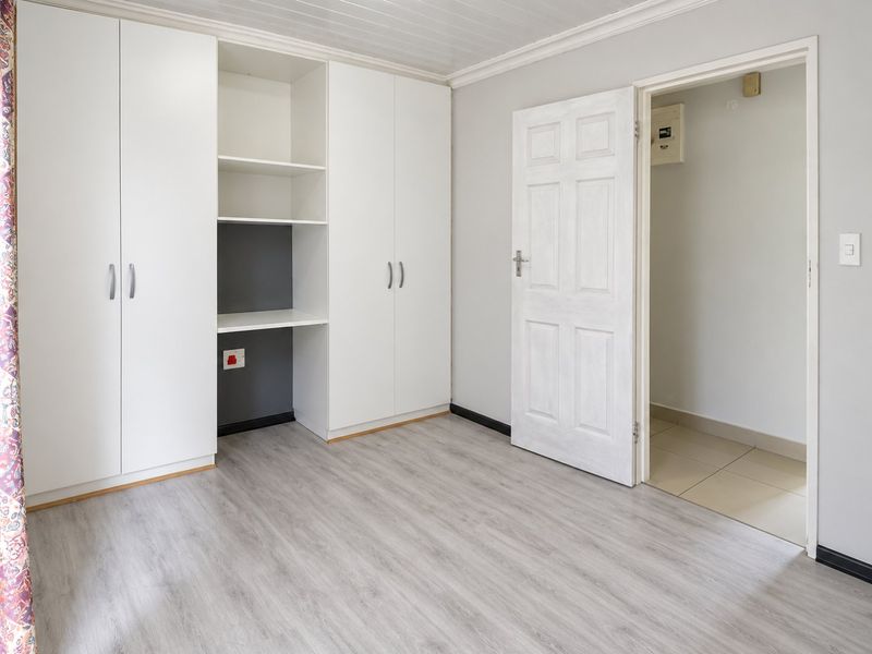 A clean, empty bedroom featuring modern laminate flooring, built-in white cabinetry with integrated shelving, and a panelled ceiling.