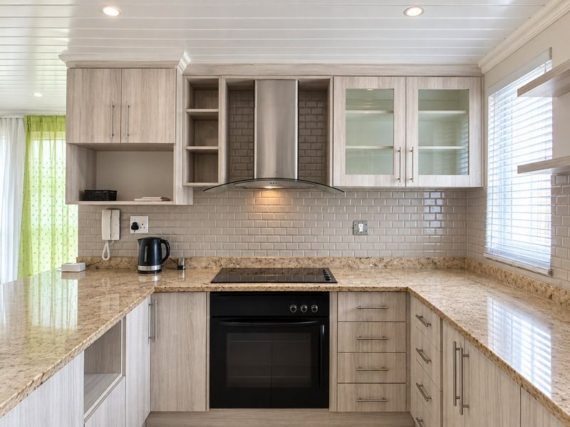 Modern kitchen featuring light wood-grain cabinetry, granite countertops, subway tile backsplash, and integrated stainless steel appliances under a clean tongue and groove ceiling.