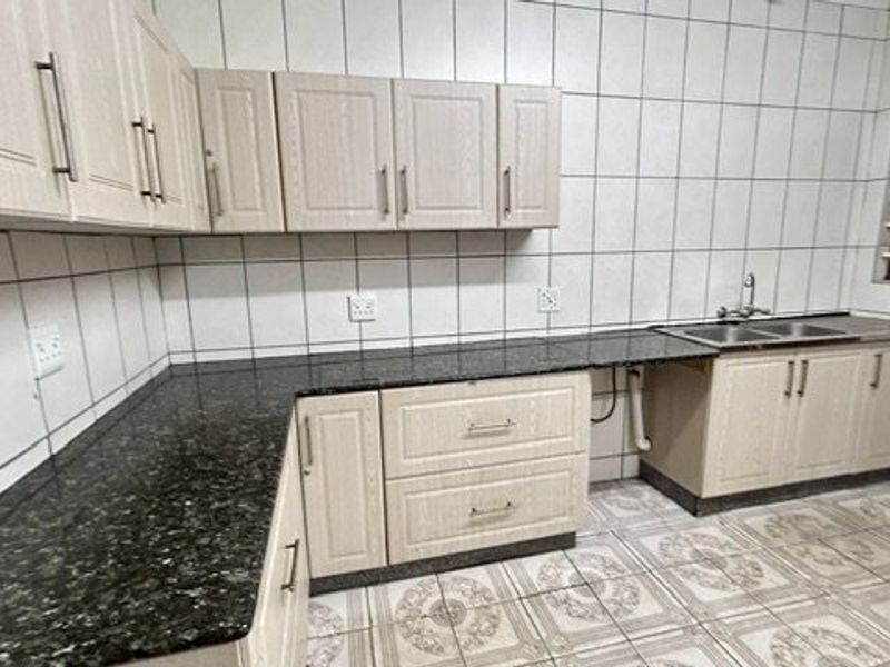 A functional kitchen featuring light-toned built-in cabinetry, dark granite countertops, a double basin sink, and full-height wall tiling.
