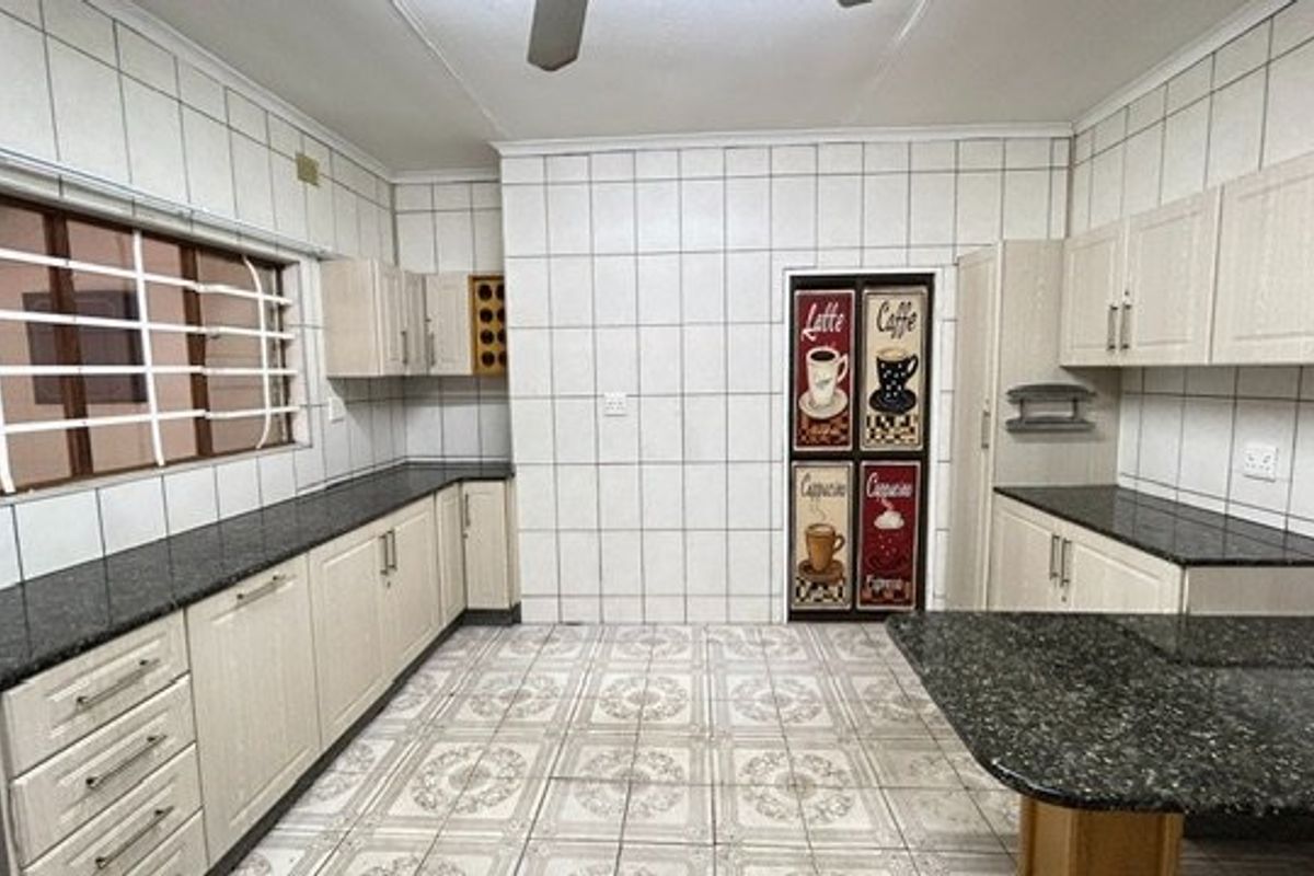 A spacious kitchen featuring granite countertops, extensive built-in cabinetry, and full-height wall tiling, offering a functional layout ready for modernization.