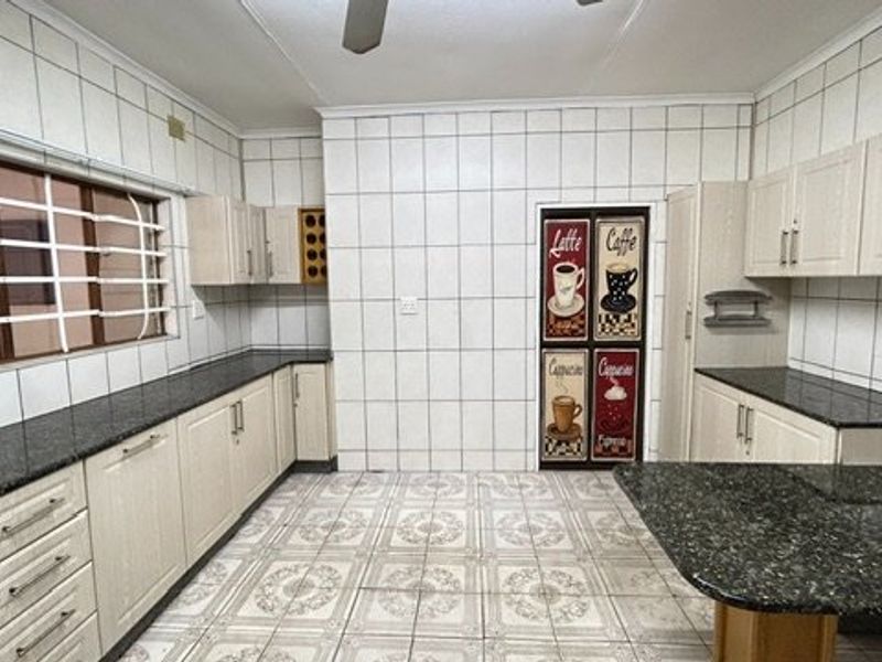 A spacious kitchen featuring granite countertops, extensive built-in cabinetry, and full-height wall tiling, offering a functional layout ready for modernization.