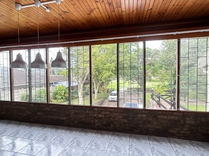 Enclosed patio area featuring a timber ceiling, tiled flooring, and large windows with security bars overlooking the garden.