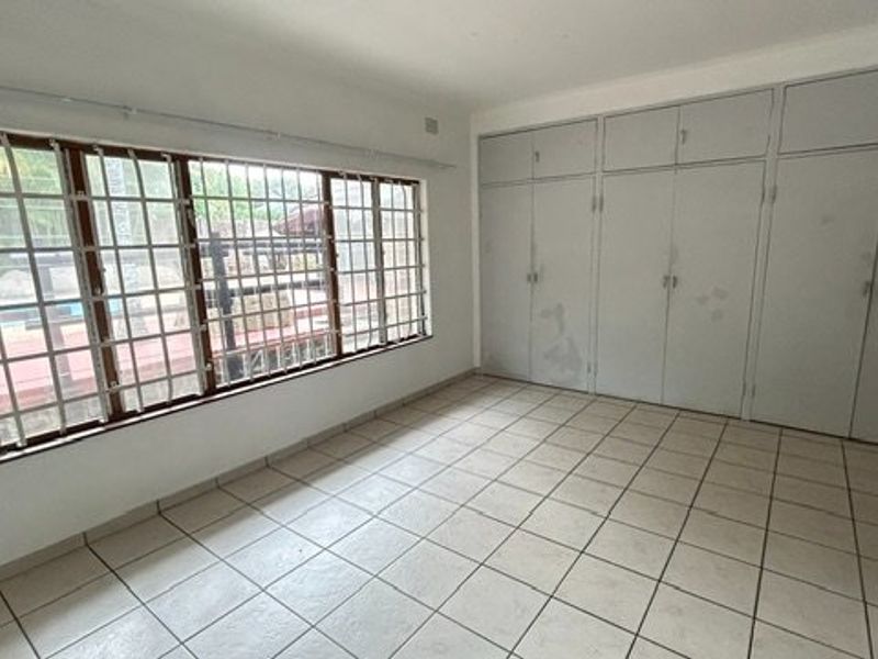 An empty bedroom featuring tiled flooring, built-in cupboards, and large windows fitted with security bars.