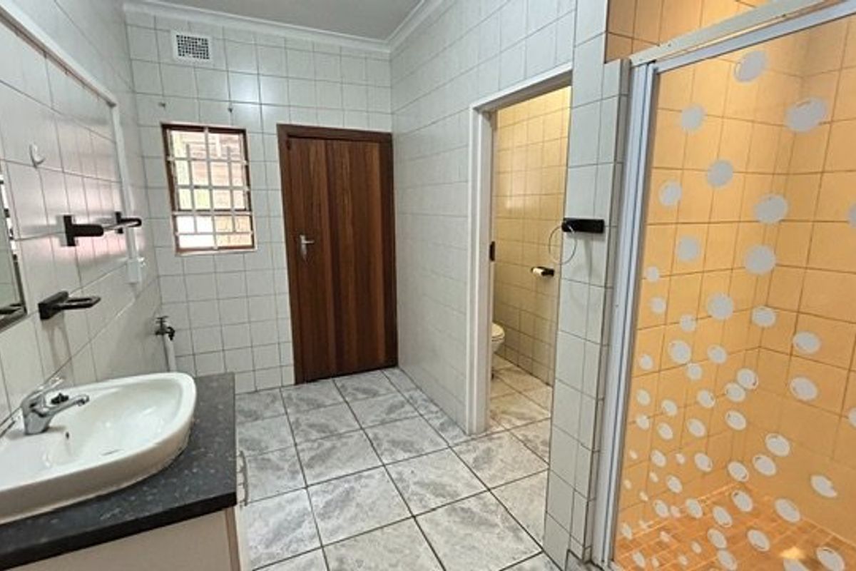 A functional bathroom featuring a vanity basin, separate shower enclosure, and a private toilet cubicle with neutral tiled finishes throughout.
