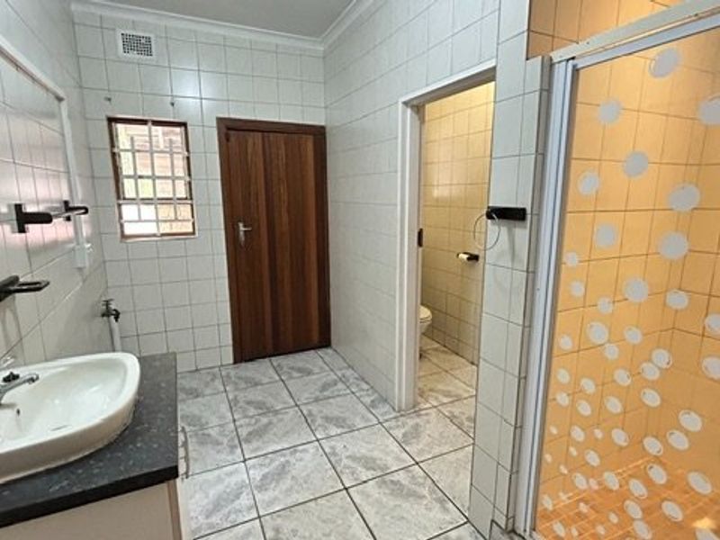 A functional bathroom featuring a vanity basin, separate shower enclosure, and a private toilet cubicle with neutral tiled finishes throughout.