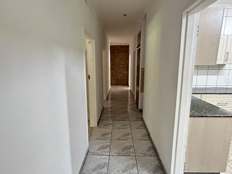 A long, tiled hallway providing access to multiple rooms, featuring a stone accent wall at the end and neutral wall finishes.