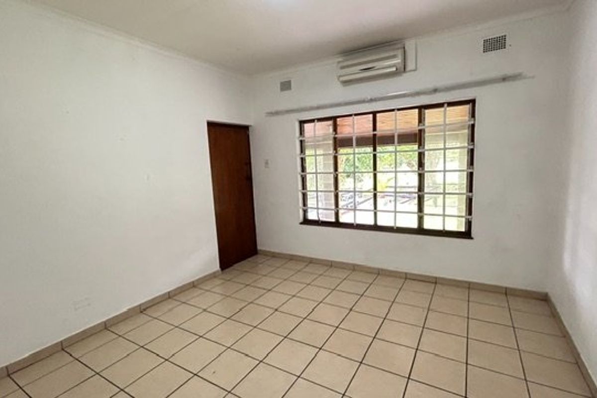An empty bedroom featuring tiled flooring, a wall-mounted air conditioning unit, and a window fitted with security bars.