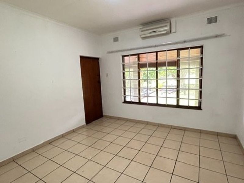 An empty bedroom featuring tiled flooring, a wall-mounted air conditioning unit, and a window fitted with security bars.