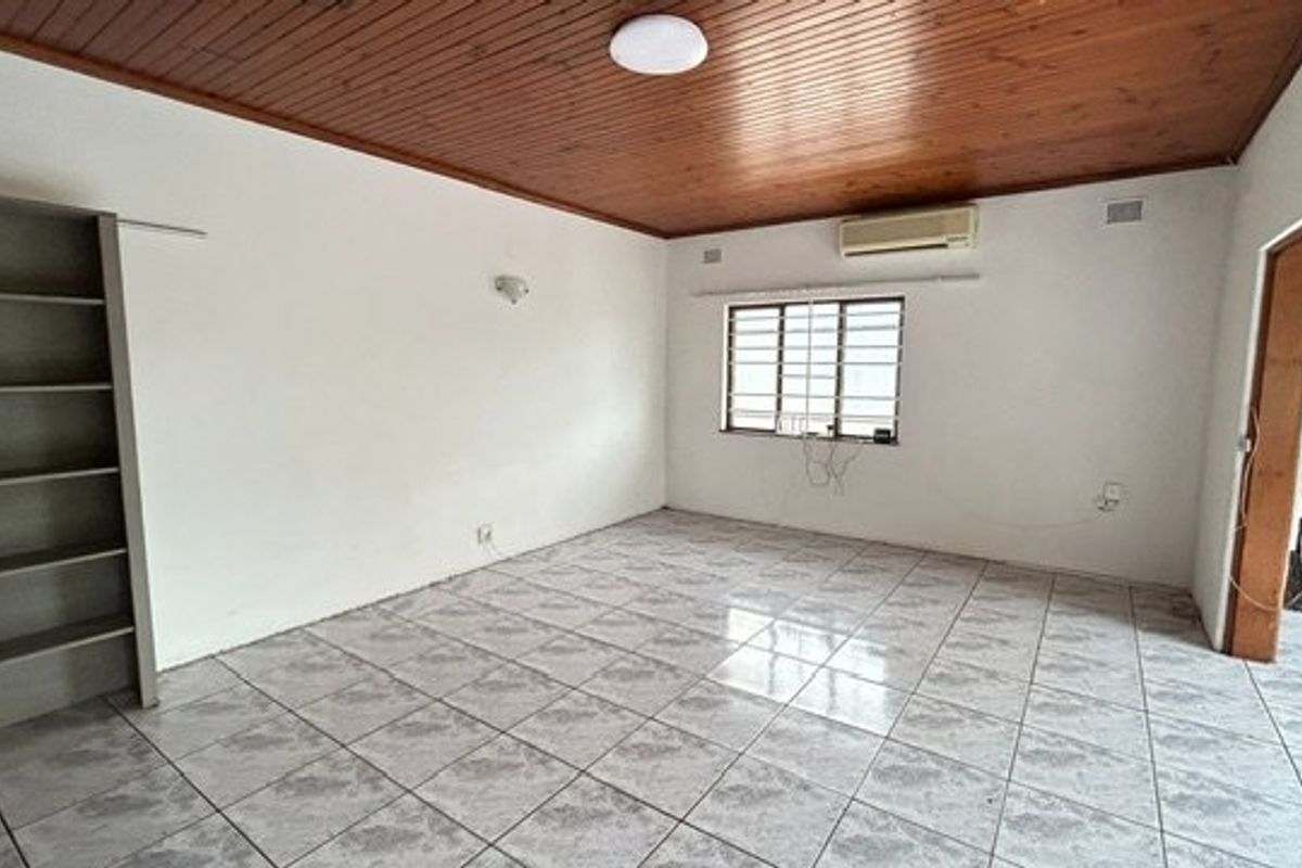 An empty living room featuring tiled flooring, a timber-clad ceiling, built-in shelving, and an installed air conditioning unit.
