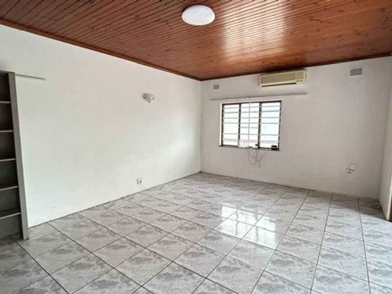 An empty living room featuring tiled flooring, a timber-clad ceiling, built-in shelving, and an installed air conditioning unit.