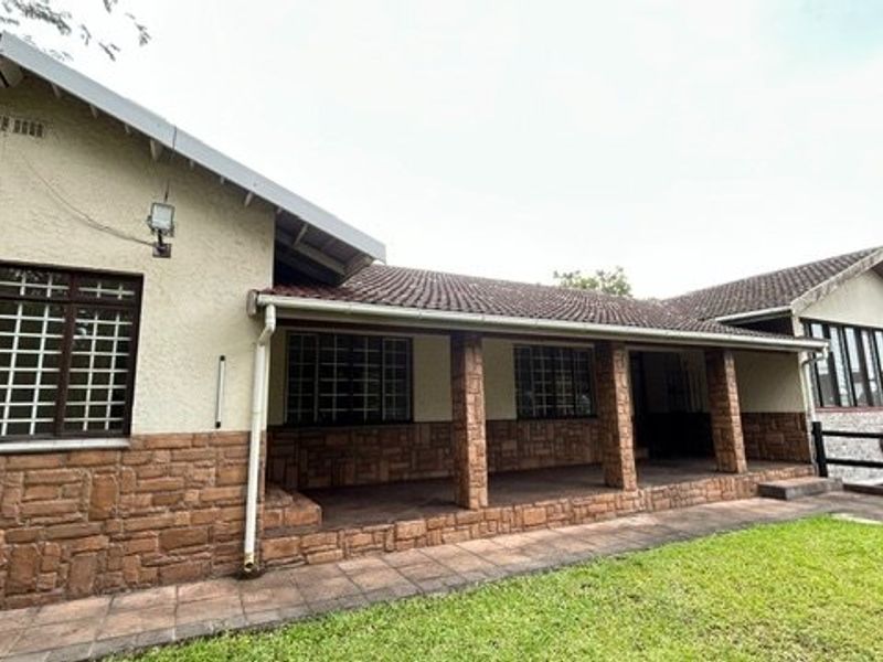 Rear view of the house featuring a covered patio, stone cladding accents, tiled roof, and security bars on the windows.