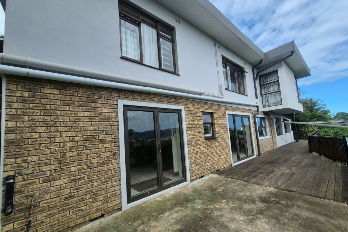 Rear exterior view of the apartment featuring a brick facade, timber decking, and multiple aluminium-framed glass doors providing access to the interior.