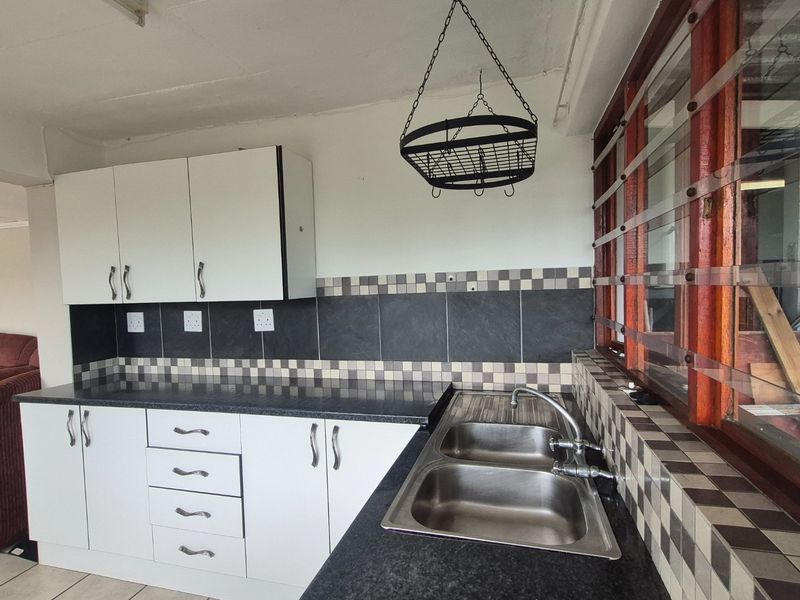 Functional kitchen featuring white cabinetry, dark laminate countertops, a double stainless steel sink, and a decorative tiled splashback.