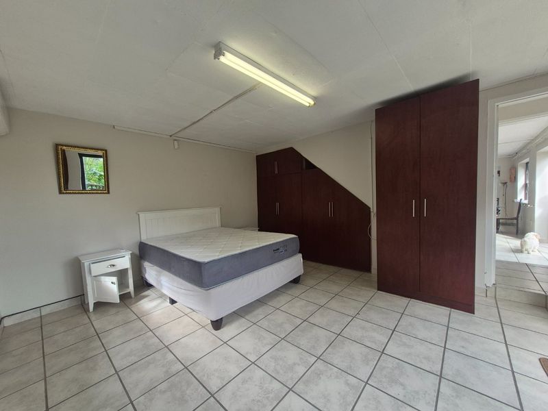Spacious bedroom featuring built-in wooden cupboards, tiled flooring, and direct access to an adjacent hallway.
