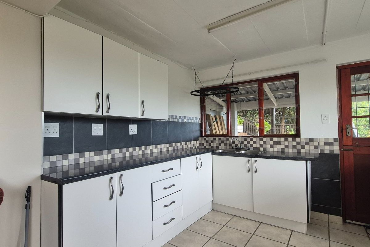 A functional kitchen featuring white built-in cabinetry, dark laminate countertops, a tiled backsplash, and ceramic floor tiles with direct access to the exterior.