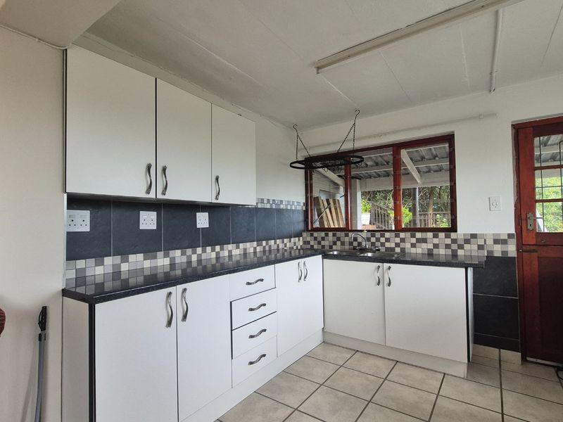 A functional kitchen featuring white built-in cabinetry, dark laminate countertops, a tiled backsplash, and ceramic floor tiles with direct access to the exterior.