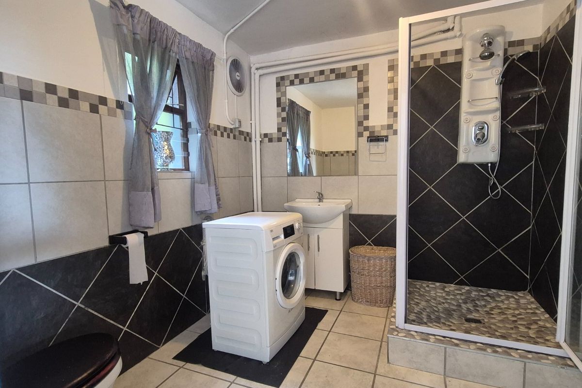 A functional bathroom featuring a shower enclosure with a modern shower panel, a pedestal basin, and integrated laundry space with tiled finishes.