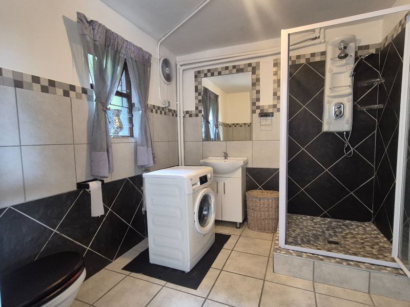 A functional bathroom featuring a shower enclosure with a modern shower panel, a pedestal basin, and integrated laundry space with tiled finishes.