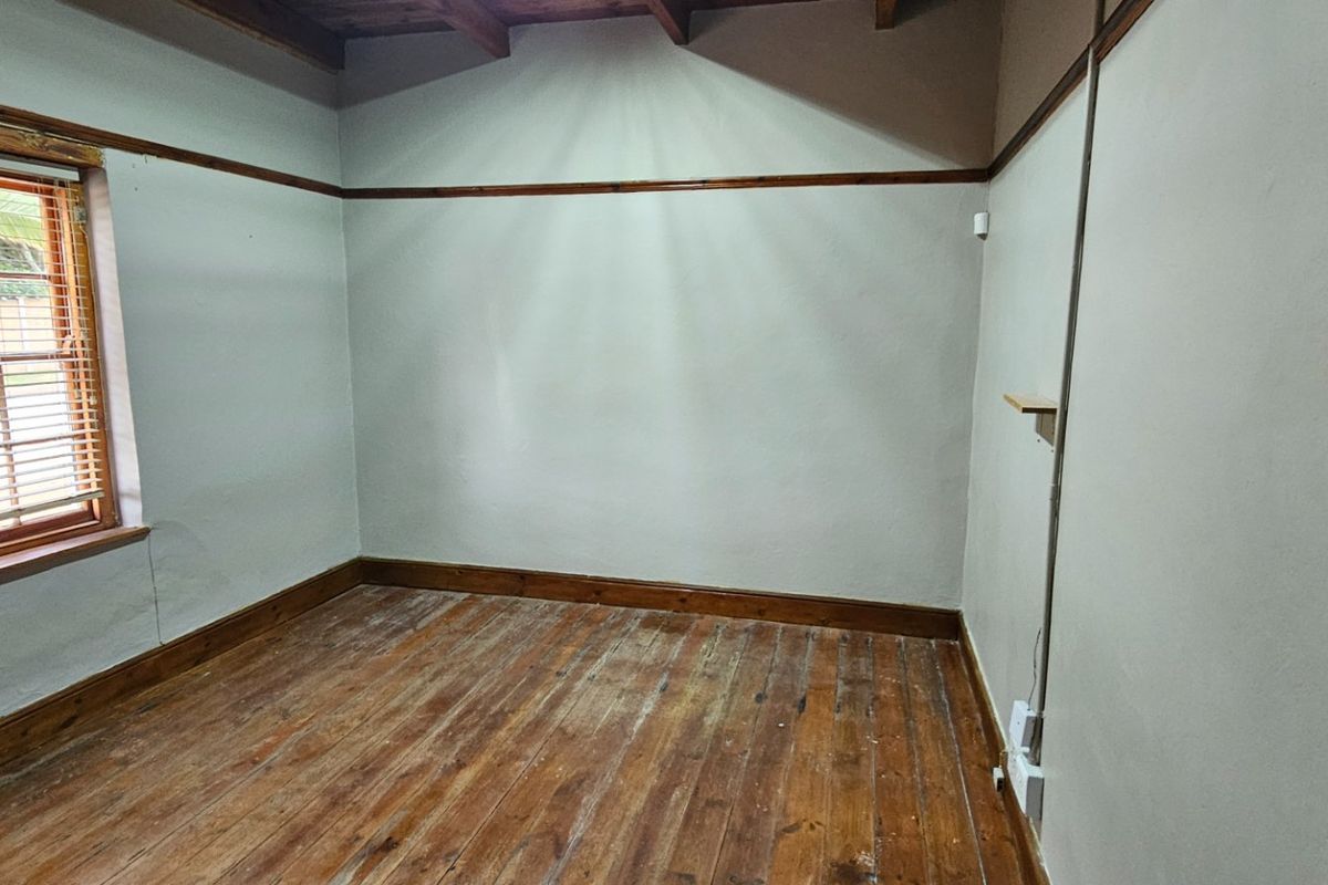 An empty bedroom featuring exposed timber ceiling beams, original timber flooring, and a window with timber frames.