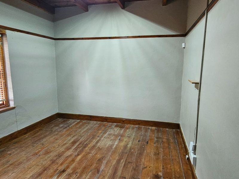 An empty bedroom featuring exposed timber ceiling beams, original timber flooring, and a window with timber frames.