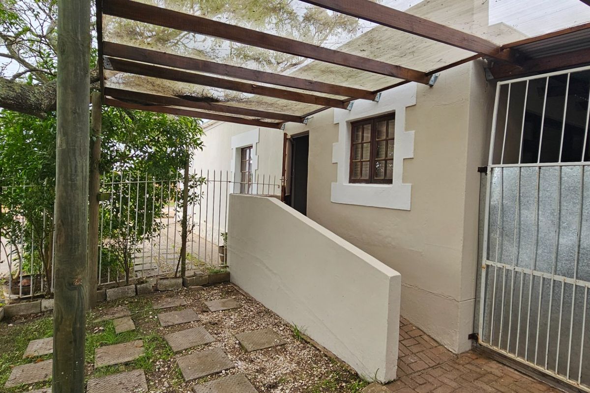 Rear exterior area featuring a timber pergola, paved walkway, and secure access gate with security bars on windows.