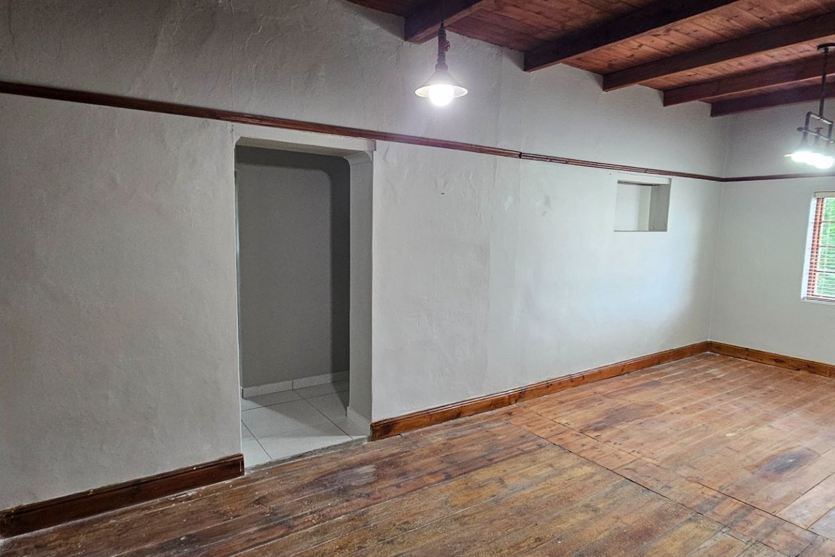An empty living area featuring exposed timber ceiling beams, original timber flooring, and classic picture rails, offering a rustic blank canvas.