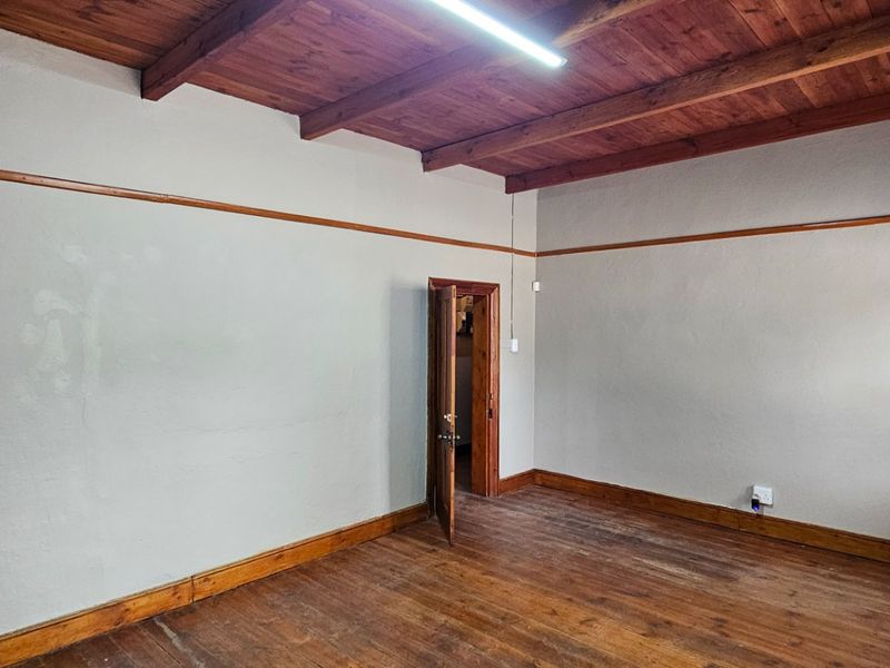 An empty bedroom featuring exposed timber ceiling beams, original timber flooring, and classic timber trim details, offering a blank canvas for renovation.