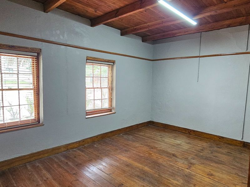 A vacant office space featuring exposed timber ceiling beams, original timber flooring, and classic timber window frames with natural light.