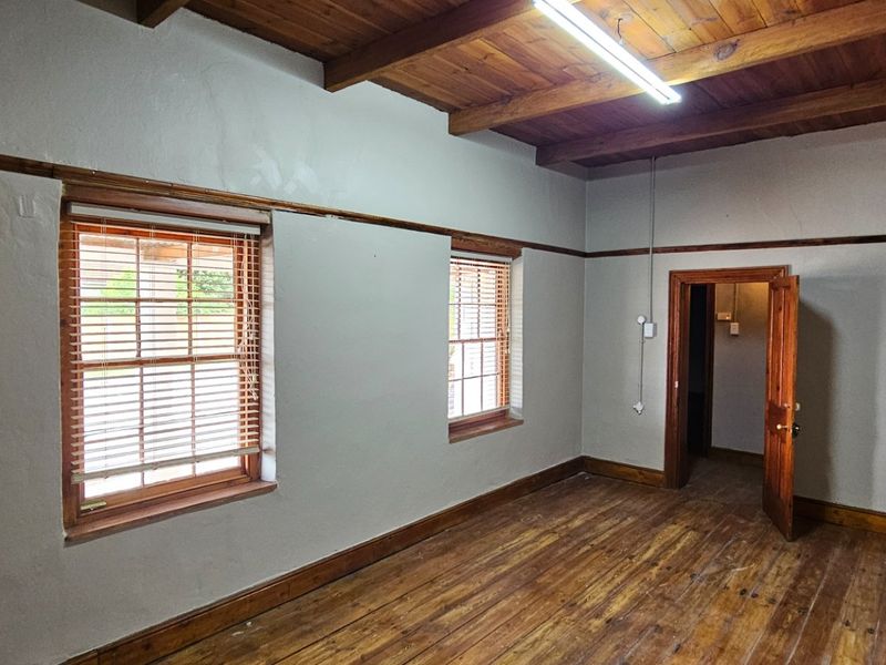 An empty office space featuring exposed timber ceiling beams, polished timber flooring, and natural timber window and door frames.