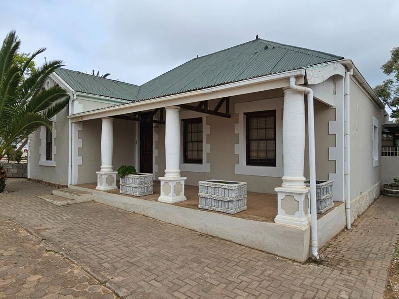 Front elevation of a commercial property featuring a covered veranda with classical columns, corrugated metal roofing, and paved exterior access.