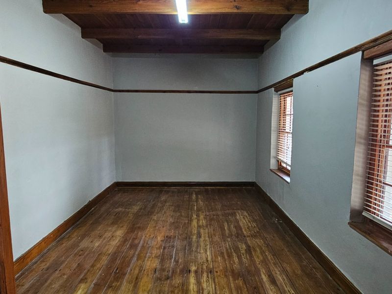 An empty office space featuring exposed timber ceiling beams, original timber flooring, and timber window frames with fitted blinds.