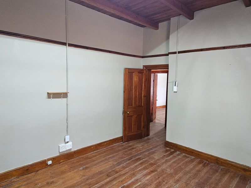An empty office space featuring exposed timber ceiling beams, original timber flooring, and classic timber door frames.