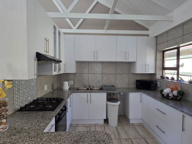 Modern kitchen featuring white cabinetry, granite countertops, gas hob, built-in oven, and exposed timber ceiling trusses, offering a clean and functional workspace.