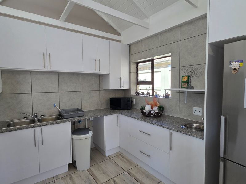 A functional kitchen featuring white cabinetry, granite countertops, a double stainless steel sink, and a vaulted ceiling with exposed rafters.