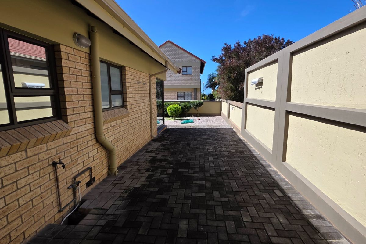 A side exterior walkway featuring paved flooring, a high boundary wall, and external utility fixtures along the townhouse brick facade.