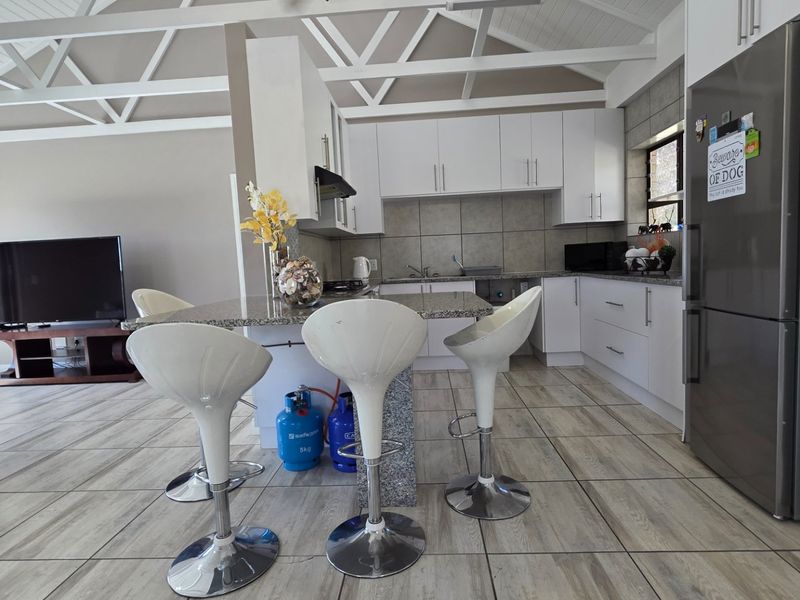 Open plan kitchen and living area featuring white cabinetry, granite countertops, tiled flooring, and exposed roof trusses.