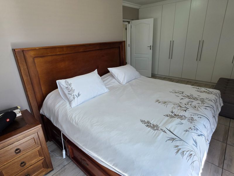 A well-maintained bedroom featuring neutral wall tones, tiled flooring, and extensive built-in cupboard storage.