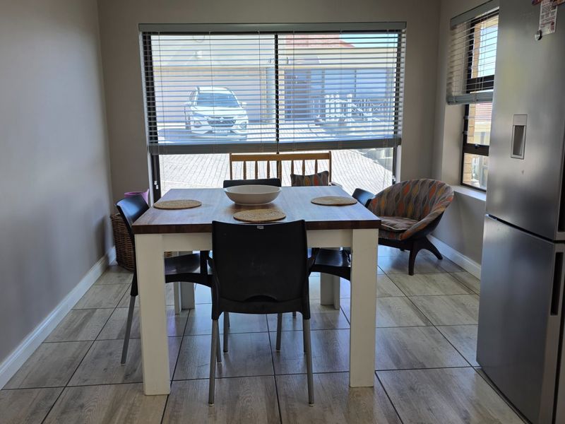 A dining area featuring neutral wall tones, tiled flooring, and large windows with venetian blinds, providing a bright and functional space for meals.