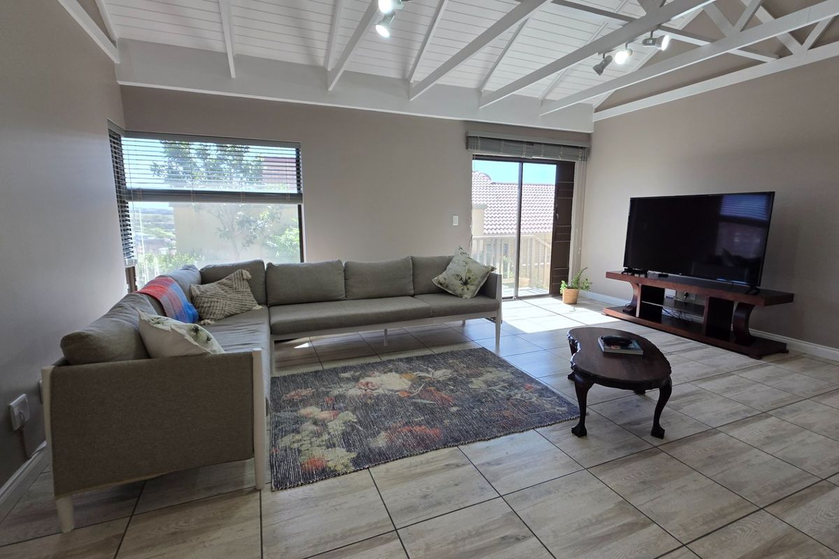 Spacious living room featuring vaulted ceilings with exposed rafters, tiled flooring, and a sliding glass door providing access to the outdoor area.