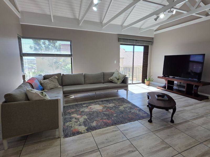 Spacious living room featuring vaulted ceilings with exposed rafters, tiled flooring, and a sliding glass door providing access to the outdoor area.