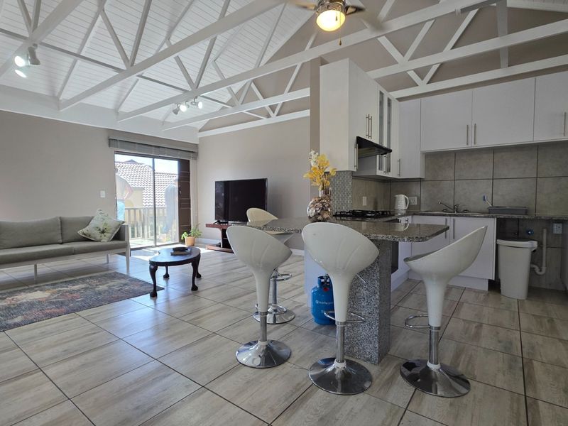 Spacious open-plan living area featuring a vaulted ceiling with exposed trusses, tiled flooring, and a modern kitchen with granite countertops.