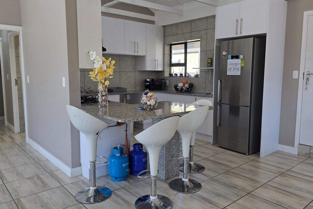 A functional kitchen featuring granite countertops, white cabinetry, a tiled backsplash, and a breakfast bar area with tiled flooring throughout.