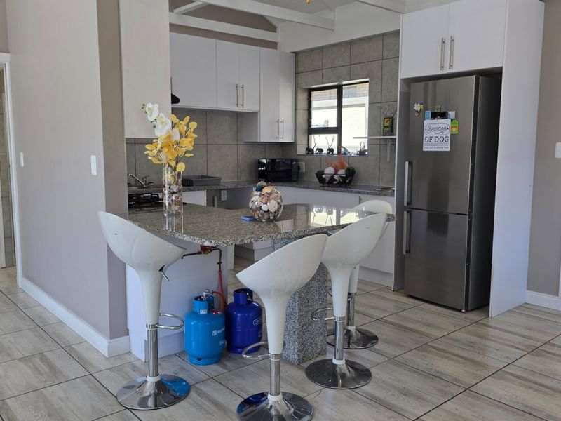 A functional kitchen featuring granite countertops, white cabinetry, a tiled backsplash, and a breakfast bar area with tiled flooring throughout.